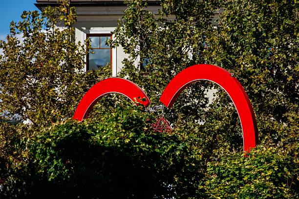 Red arch sculpture amidst lush greenery in urban park setting, lifestyle