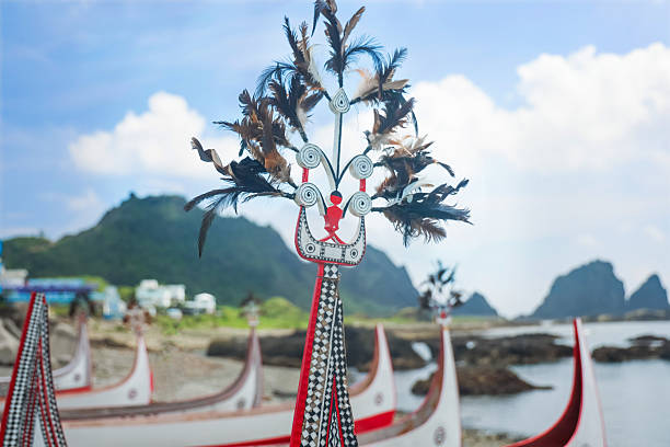 Traditional Tao canoe with red and white decorations standing on a rocky shore of Orchid Island Taiwan with blue sky and sea in the background