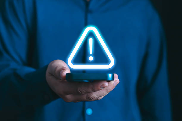 istock Glowing warning alert icon with exclamation sign displayed above a smartphone in hand. Concept of mobile security risk, system error, malware alert, cyber threat, and data protection caution of spam 2234682802