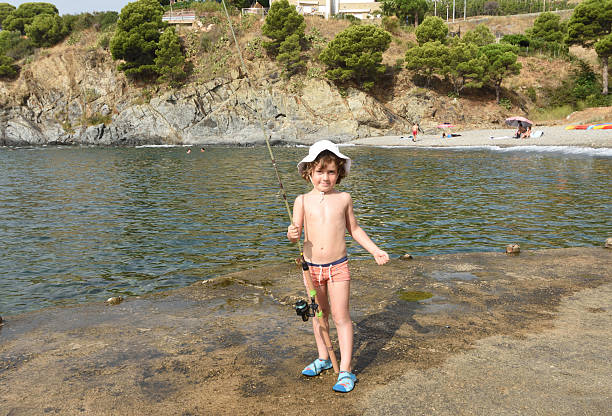 A young boy fishes in crystal clear emerald waters.