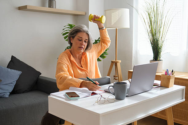 istock Mature businesswoman lifting dumbbell while working at home office desk 2234697002