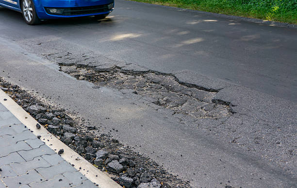 istock Car driving towards a large pothole in asphalt near curb, visible surface damage and broken road edges. 2234697008