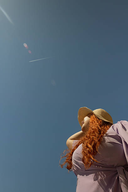 istock Red haired woman wearing a summer hat looking at the sky on a sunny day, low angle view 2234698108