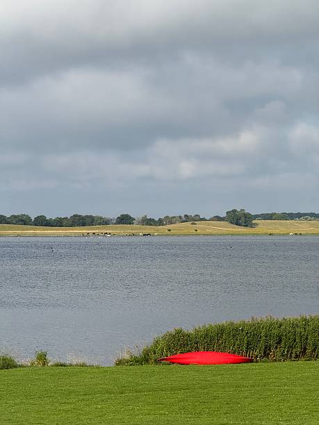 A red canoe rests on the grass by the shore of Roskilde Fjord with towering clouds in the background