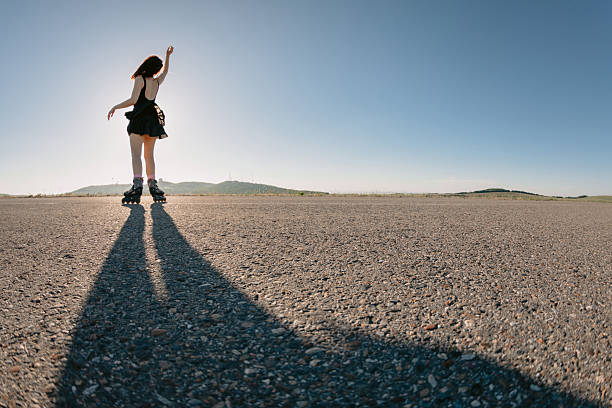Woman roller skating on empty road at sunset, long shadow on asphalt, freedom and active lifestyle