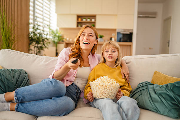 istock Mother and daughter watching television and eating popcorn on sofa 2234708509