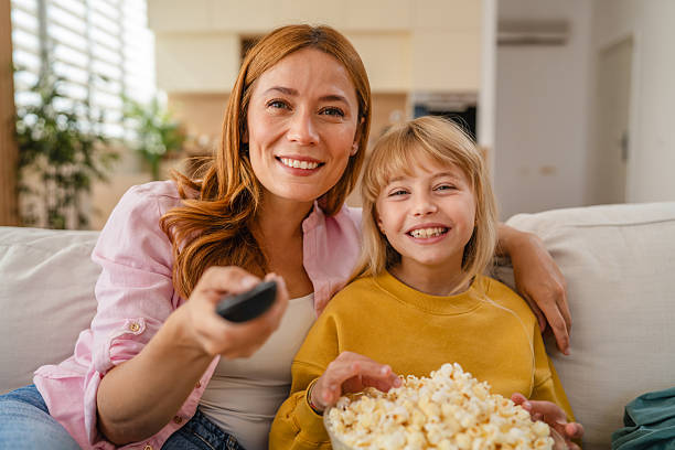 istock Mother and daughter watching television and eating popcorn on sofa 2234709274