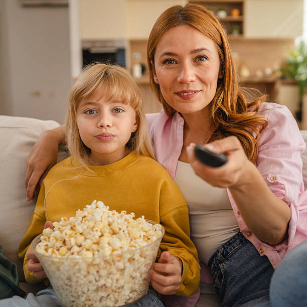 istock Mother and daughter watching television and eating popcorn on sofa 2234709418