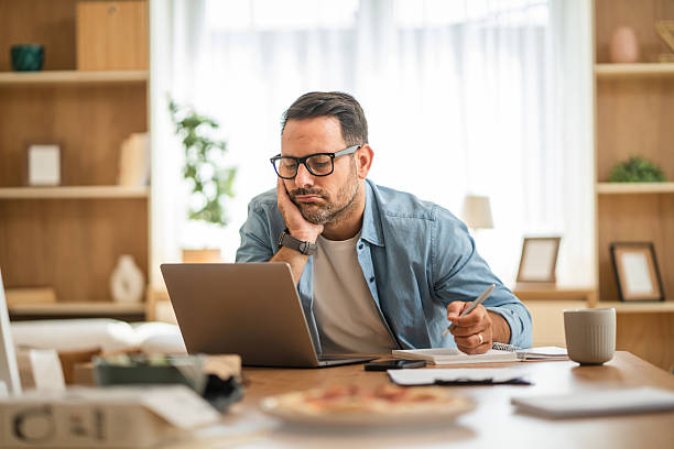 istock Tired freelancer taking notes and looking at laptop at home 2234710315