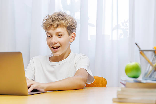 istock Schoolboy studying at home with a laptop, smiling with a joyful expression 2234713561