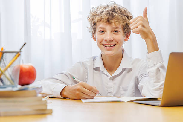 istock Schoolboy studying at home with laptop, notebook, and learning materials, smiling happily 2234713580