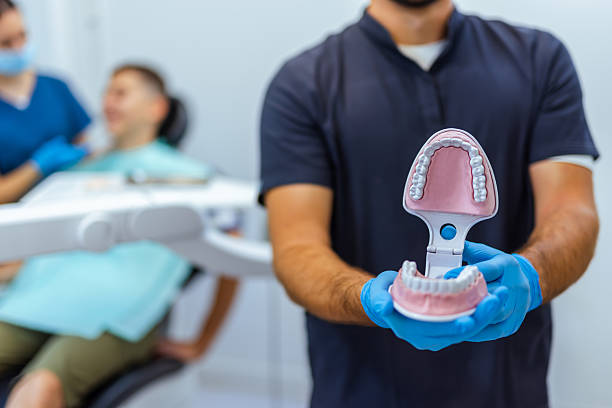 Dental Doctor Holding Jaw Model with Nurse Treating Boy in Background Portrait of dental doctor holding a jaw model while nurse treats a boy in the blurry background, showing professional pediatric dental care and education. dentist stock pictures, royalty-free photos & images