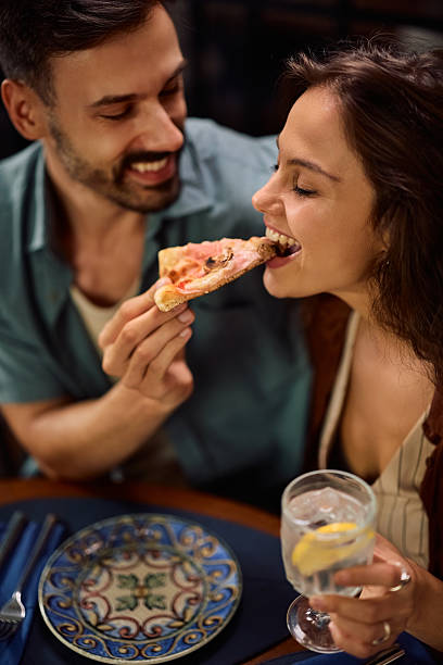 istock Happy man feeding his girlfriend with pizza during a lunch in pizzeria. 2234718421