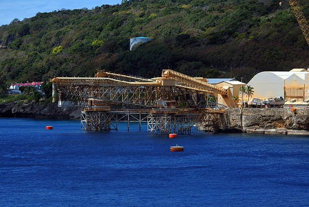 Flying Fish Cove, Christmas Island: large large steel cantilever loading systems were constructed to facilitate the export of phosphate, the island’s principal resource. These structures extend from the shore over deep water, allowing bulk carriers to be directly loaded from conveyor belts transporting phosphate from inland stockpiles. The cantilevers are a key element of the island’s mining infrastructure, reducing reliance on smaller vessels and streamlining shipping operations. The phosphate industry on Christmas Island, has been a cornerstone of the island’s economy since 1899. Low-grade rock phosphate is extracted, primarily for export as fertilizer to Southeast Asian markets, with over 16 million tonnes shipped since operations began. Employing approximately 300 full-time workers, the industry contributes around $30 million annually to the local economy, representing 40% of the island’s labor force. However, with mining leases set to expire in 2034 and a 2018 federal rejection of expansion plans due to environmental concerns, particularly regarding the island’s unique biodiversity and red crab population, the industry faces an uncertain future.
