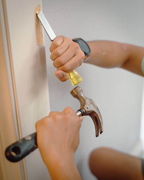 istock Two hands shape hinge recess on wood trim with yellow-handled chisel and hammer. Black smartwatch visible. Close-up captures finishing technique in DIY carpentry. Wall-mounted mortise in progress 2234729231