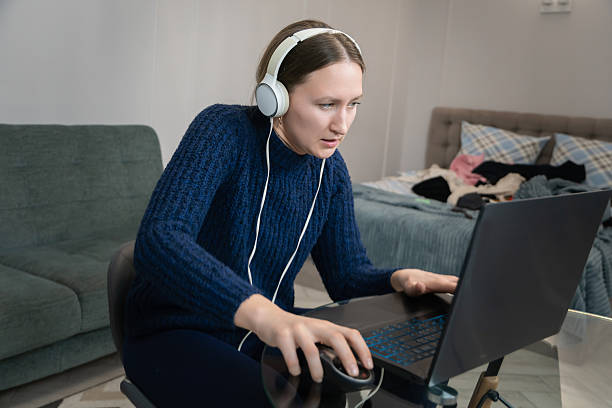 istock Young woman wearing headphones is working or studying from home, using laptop and mouse, concentrating on the screen while sitting in her messy bedroom 2234729868