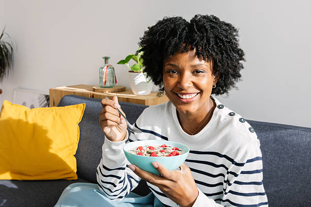 istock Happy young black woman eating healthy breakfast bowl sitting on sofa at home 2234732060