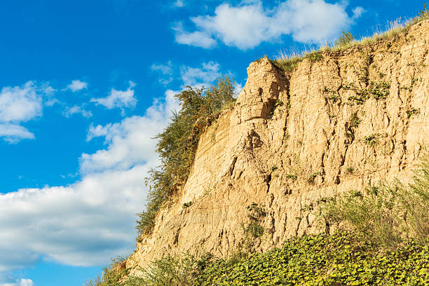 istock Sunlit sandy cliff with sparse vegetation against a vibrant blue sky with fluffy clouds, showcasing natural erosion and rugged landscape in a bright, clear day. 2234735991