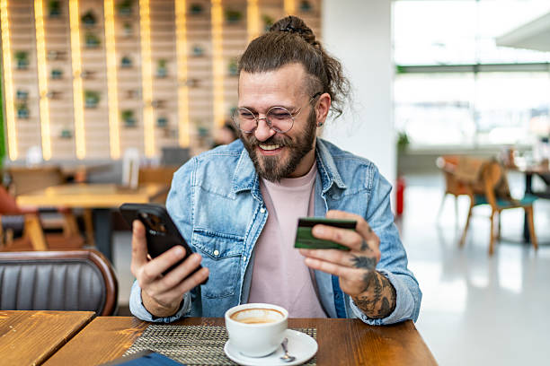 istock Smiling young man making online payment using credit card and smartphone in cafe 2234741288