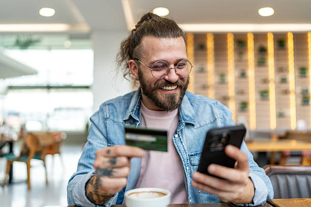 istock Smiling man making online payment using credit card and smartphone in cafe 2234741300