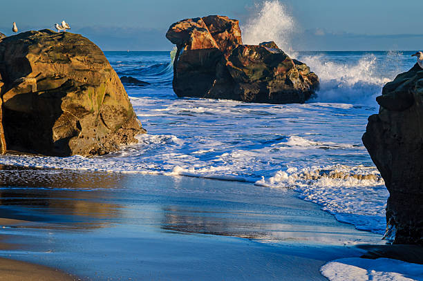 Ocean waves crashing on rocky sea stumps along a Pacific Ocean beach.\n\nTaken in Santa Cruz, California, USA