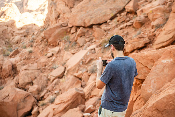 This is a photograph of a man in his 40s wearing a baseball hat while stopping to take photos with his mobile phone in the Nevada desert on a summer day.