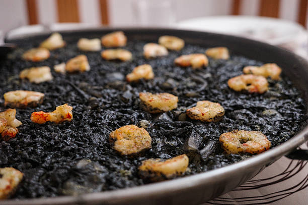 Close-up of a homemade Spanish black rice paella with prawns, prepared with squid ink and seafood, served in a traditional paella pan. Typical Mediterranean cuisine concept