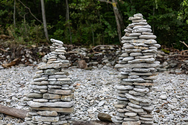 Stone towers on rocky Ontika beach, Estonia. Carefully balanced limestone stacks on pebble shore with driftwood, forest trees in background. Overcast summer weather, calm and natural coastal scene.