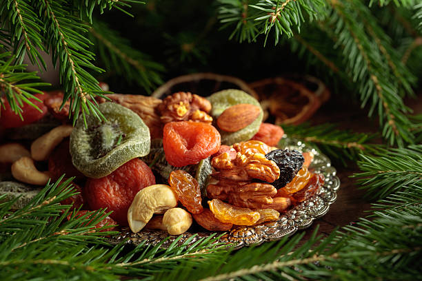 Assorted dried fruits and nuts on a silver tray. Vegetarian dessert and Christmas tree branches on an old wooden table.