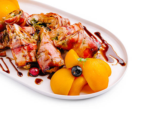 A gourmet plate showcases bacon-wrapped rolls, beautifully arranged with a garnish of peach slices and berries. This vibrant dish highlights creativity and flavor balance.