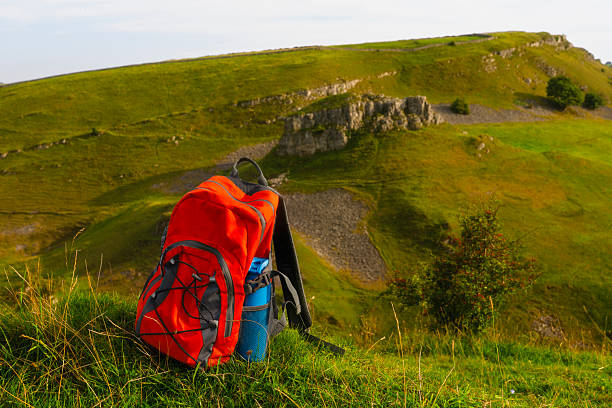 Vibrant red backpack sits on lush green grass, surrounded by rolling hills and rocky formations under soft evening light, ideal for hiking adventures.