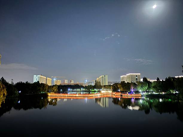 This picture shows a quiet city night scene. In the picture, the wide water surface occupies the lower part, as calm as a mirror, reflecting the lights of the tall buildings on the other side. The high-rise buildings are scattered in height, and the light shines through the windows, forming patches of flickering light, which appear particularly bright against the dark sky. The overall atmosphere is quiet and warm, showing the unique charm of the city at night.