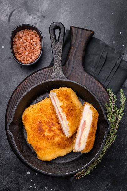 Fried cordon bleu cutlet with cheese and ham in pan. black background. top view