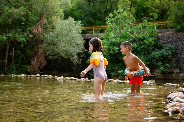 Two young children are enjoying a refreshing swim in a clear river on a summer day