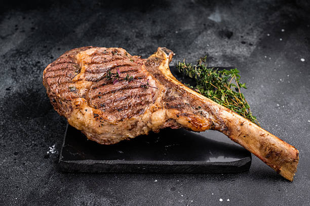 istock BBQ Grilled Tomahawk beef steak, cooked rib eye with bone on marble board. black background. top view 2234806469