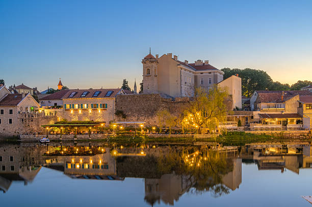 Twinkling lights illuminate Trebinje's riverside as sunset casts a golden glow over the landscape.