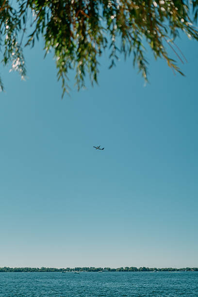 Commercial airplane flying high above Toronto against a clear blue sky. Represents air travel, transportation, tourism, and the concept of global connectivity.