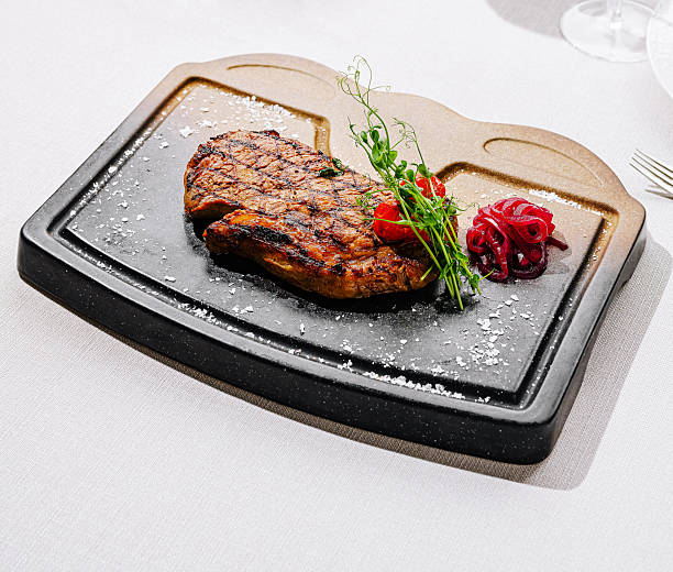 A perfectly grilled steak sits on a hot stone plate, accompanied by fresh herbs and roasted vegetables. The vibrant colors and sizzling sound create an appetizing dining experience.