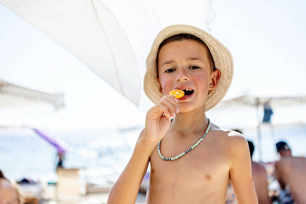 A joyful child savoring a lollipop on a warm beach under a bright summer sun, evoking carefree vacation vibes and happiness.