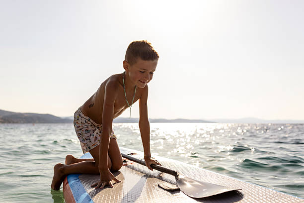A joyful boy paddles on a paddleboard in a serene and sunny seascape.