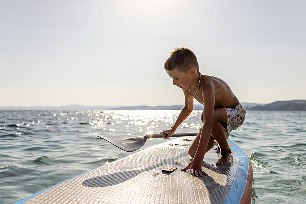 A young boy balances and paddles on a paddleboard in open tranquil waters, enjoying the sunshine.