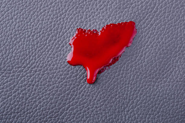 A vivid red paint or nail polish drop splattered on a gray textured surface, creating an artistic contrast. The setting emphasizes texture and color in a minimalist way, inviting interpretation.