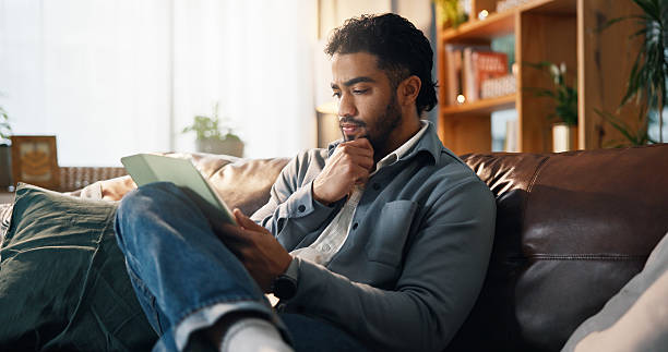 istock Home, thinking and man on sofa, tablet and online reading with connection, ideas and relax. Apartment, ebook and person with tech, choice and internet with review for novel, website info and decision 2234814786