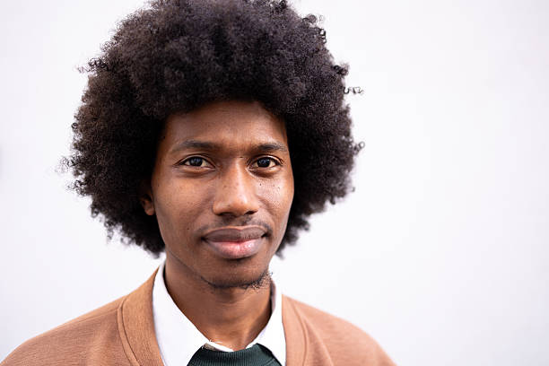 A person wearing a casual sweater and shirt smiles gently while standing outdoors. The background is neutral, creating a minimalist profile ideal for professional or personal use.