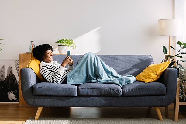 istock Joyful black woman relaxing on sofa using smart phone on sunny winter day 2234823005