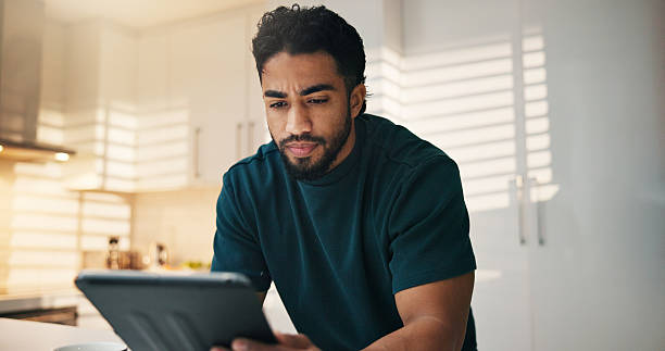 istock Tablet, reading and man in kitchen in morning with networking, communication or mobile app in home. Digital technology, research and male person thinking for texting, contact or social media in house 2234824723