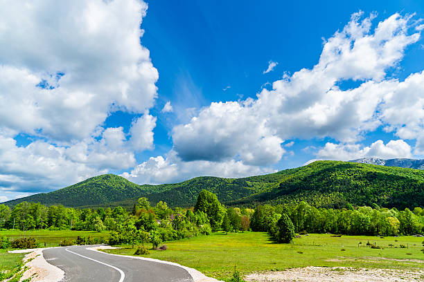 istock Curved Road Leading through Green Fields and Hills under Blue Sky with White Clouds in Croatia 2234825348