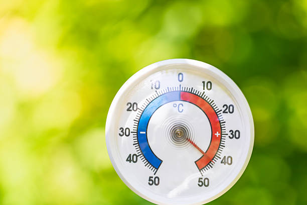 An analog outdoor thermometer shows a high temperature of nearly 45C degree on a sunny summer day, with a green blurred garden background indicating heatwave or extreme weather conditions