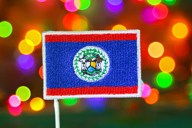 Embroidered Belize national flag displayed in front of a soft colorful bokeh background, resembling fireworks and festive lights. The vibrant composition reflects Belize City’s New Year celebration, blending patriotism with joyful holiday spirit. Suitable for themes of culture, identity and seasonal festivities.
