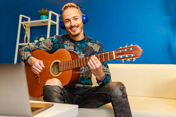 istock Young stylish caucasian man taking guitar class online at home using his laptop 2234834857